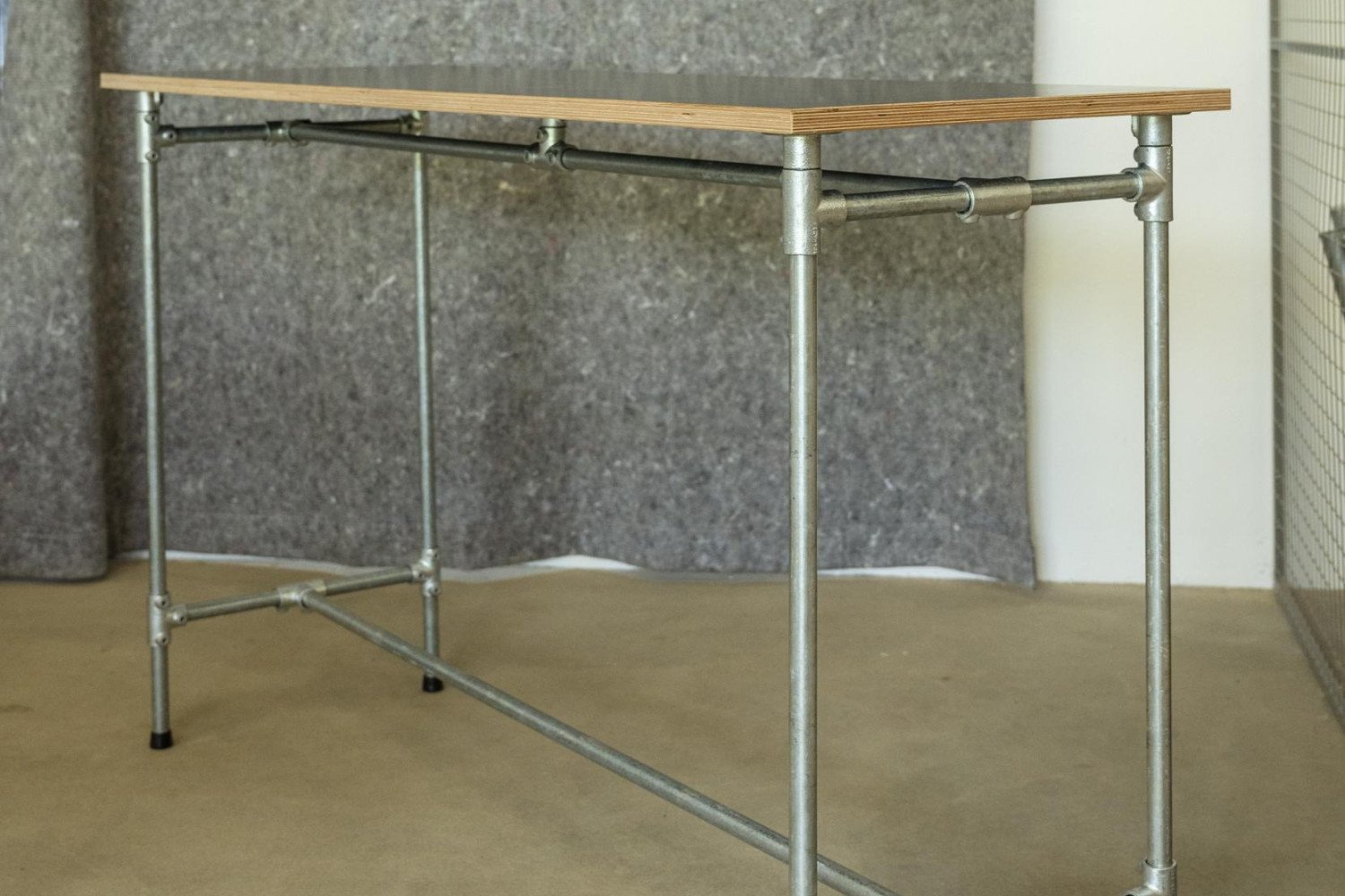 Schlichter Tisch aus Holz mit stabilen Metallbeinen vor grauer Wand. Einfache, moderne Ästhetik.