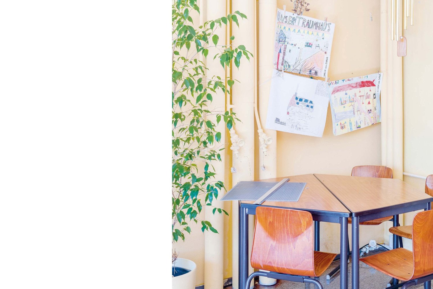 Eine Raumecke im ehemaligen Schulgebäude. Vor den Steigleitungen des Heizsystems mit großen Ventilen steht eine kleine Tischgruppe mit Stühlen.