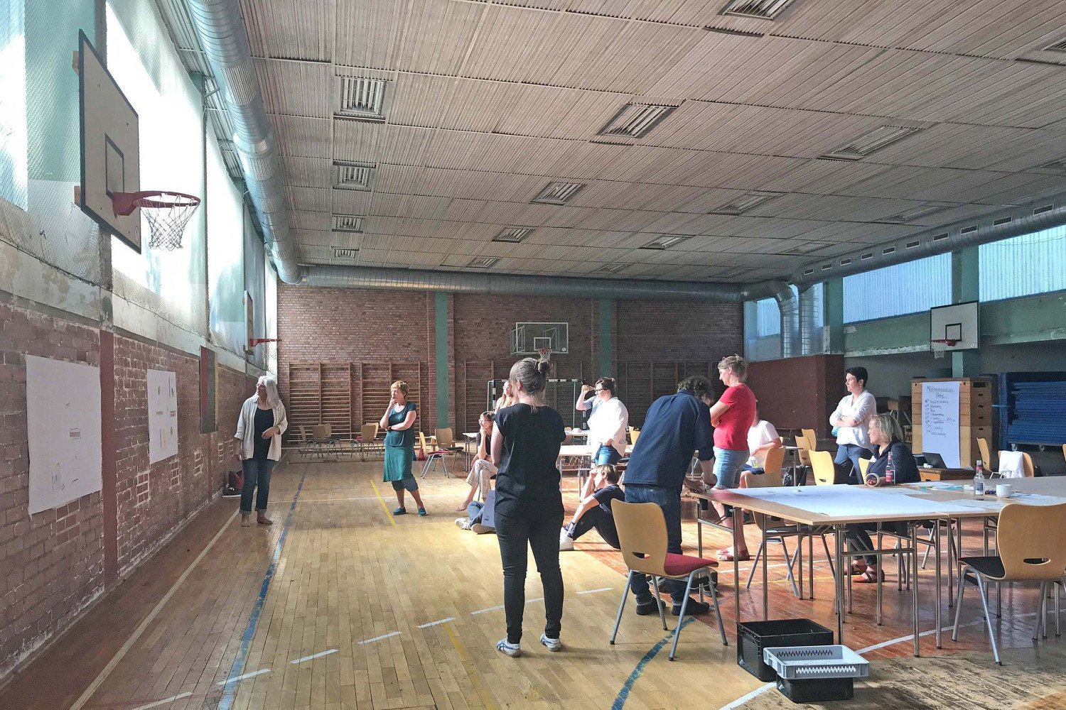 Etwa 15 Personen arbeiten in der Turnhalle an Tischen und präsentieren die Ergebnisse ihres Workshops.