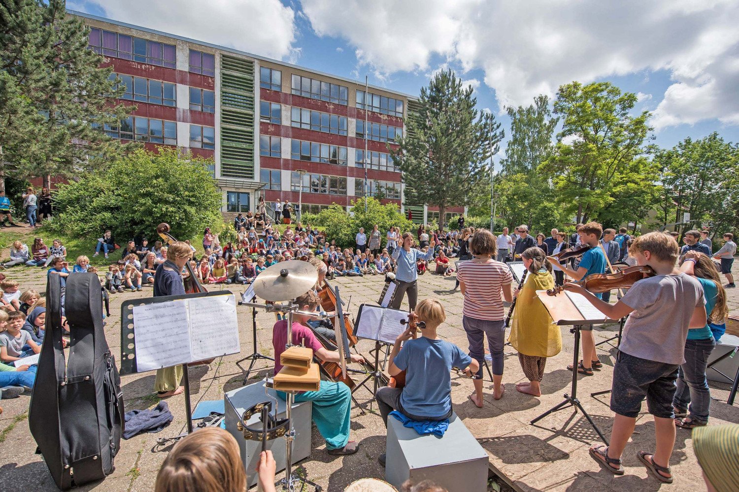 Das Schulorchester der Schule spielt bei einer Veranstaltung auf dem Schulgelände der Schule. Es ist Sommer.